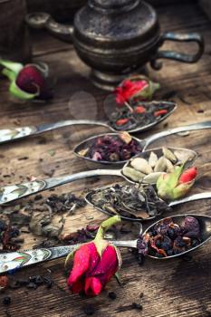 Vintage spoons with different varieties of tea on vintage wooden plank background.
