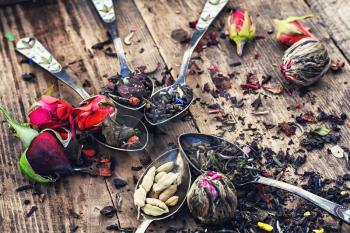 Varieties of tea brewed in an iron spoon on wooden background with buds of tea roses