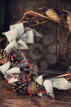 Woven from twigs and decorated with pine cones Christmas wreath on wooden background.