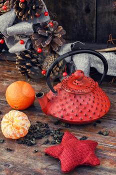 Cast iron kettle red,tangerine,tea leaves on wooden background