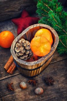 Wooden bucket with tangerines and pine cones on the background of Christmas trees and spices