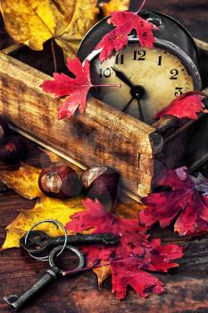 Obsolete alarm clock on wooden background strewn with fallen leaves