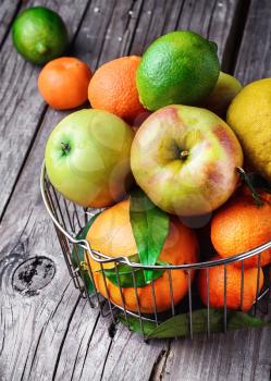 Metal fruit basket with apples and citrus fruits on the wooden table