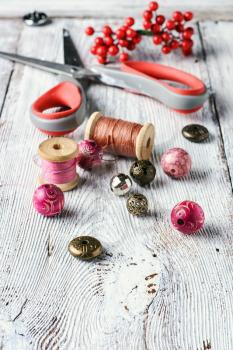 Beads,thread and scissors for needlework on a light grey wooden background