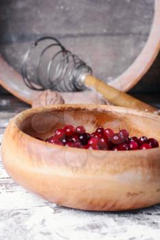 Wooden bowl with cranberries on a wooden background with kitchen smeared with flour