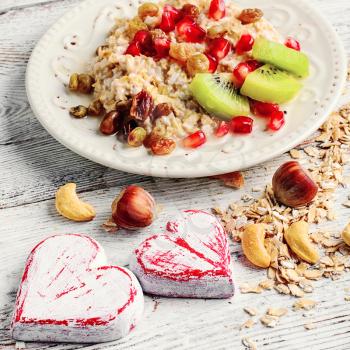 Cooked oat cereal with fruit and nuts on a background of two wooden hearts