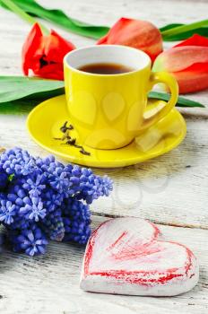 Yellow cup with tea,symbolic of the heart and a bouquet of red tulips