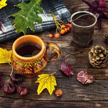 Cup of tea on the table strewn with autumn leaves and warm blanket