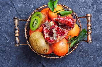 Stylish basket with tangerines,kiwi and pomegranate on slate background