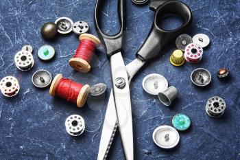 Stylish scissors for fabric,set of buttons and thread on slate dark background
