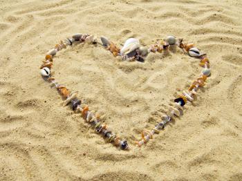 Heart from cockleshells and sea pebbles laid out on sand