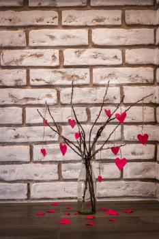 Bouquet of branches and fallen hearts on white brick wall background