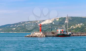 Entrance to port of Balchik resort town, red lighthouse on the pier. Coast of the Black Sea, Varna region, Bulgaria