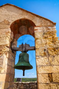 Medieval stone castle in Calafell town, Spain. Bell hanging in arch over blue sky background