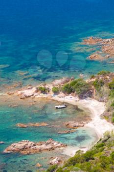 Corsica island, Cupabia gulf. Vertical coastal landscape with small motor boat near wild rocky beach