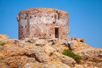 Old Genoese tower on Capo Rosso cliff, Corsica island, France. Selective focus on a foreground