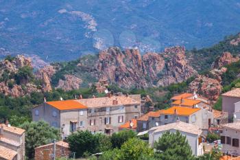 Small Corsican village landscape, old living houses with red tile roofs over mountains background. Piana, South Corsica, France