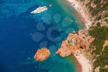 Luxury white pleasure yacht anchored near rocky beach of Corsica island, birds eye view 