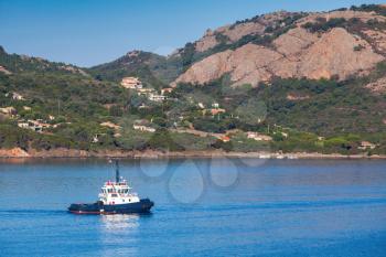 Small tug boat with white superstructure underway on Porto-Vecchio bay, Corsica island, France