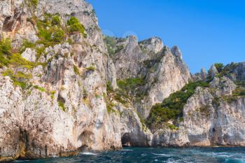 Small touristic motorboat enters the grotto in coastal rocks of Capri island, Italy