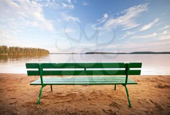 Green wooden bench in front of the lake coast