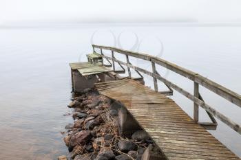 Old ruined wooden pier on the lake in foggy morning