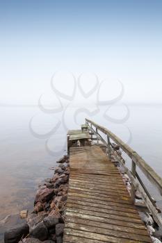 Old ruined wooden pier on Saimaa lake in foggy morning