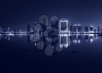 Night modern city skyline with shining lights and reflection in the water. Manama, the Capital of Bahrain, Middle East. Monochrome photo