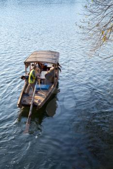 Hangzhou, China - December 5, 2014: Traditional Chinese wooden recreation boat with boatman and passengers floats on the West Lake. Famous park in Hangzhou city, China