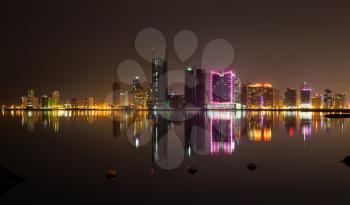 Night modern city skyline with shining neon lights and reflections in water. Manama, Bahrain, Middle East