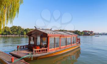Traditional Chinese red wooden water taxi boat stands moored on the West Lake coast. Famous park in Hangzhou city center, China