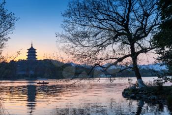 Black trees silhouette and traditional Chinese pagoda on the coast of West Lake. Famous park in Hangzhou city center, China
