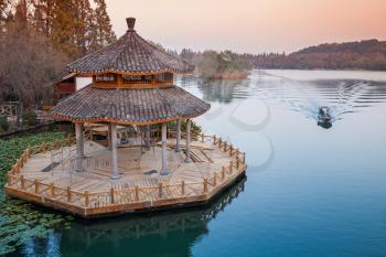 Small boat and round traditional Chinese wooden gazebo on the coast of West Lake park in Hangzhou city, China