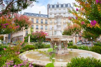 Old fountain and colorful flowers in the middle of the Place Francois 1er, Paris, France