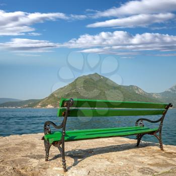 Green wooden bench stands in sunny summer morning on the seacoast in Perast town, Montenegro