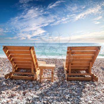 Two wooden sun loungers stand on the Adriatic Sea coast under dramatic cloudy sky