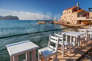 White wooden chairs and tables stand on Adriatic sea coast in Petrovac, Montenegro