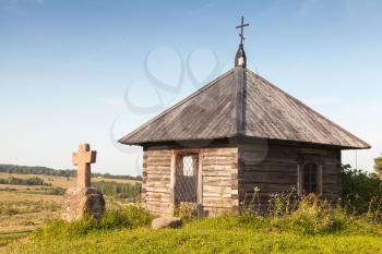 Ancient wooden Orthodox chapel and a stone cross on Savkina gorka, Pskov Region, Russia