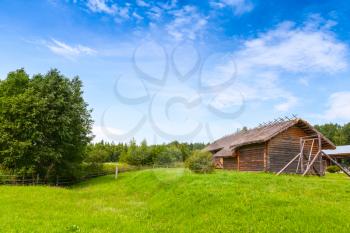 Russian rural landscape with old wooden barns on green hills under bright blue cloudy sky