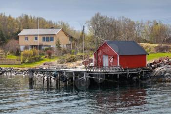 Traditional Norwegian red wooden fishing boat barn on the sea coast in spring