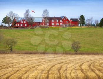 Spring rural Norwegian landscape with red house and dry field