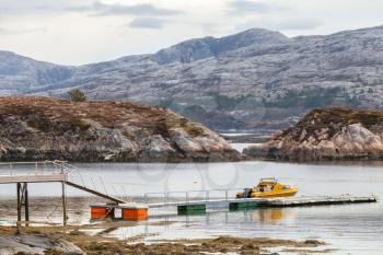Rural Norwegian coastal landscape. Small motor boat stands moored near floating pier