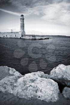 Old venetian lighthouse of Rethimno with rocks coast on foreground. Island Crete, Greece.