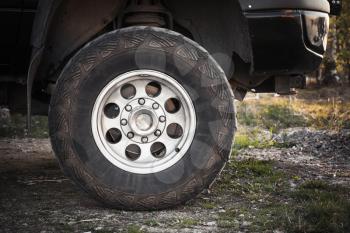 Close-up photo of SUV car wheel on dirty rural road with grass, front view