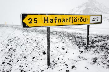 Yellow Icelandic road sign with destination and distance stands on the roadside in cold snowy winter day