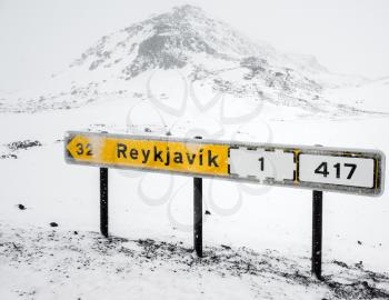 Yellow Icelandic road sign with direction and distance to Reykjavik city stands on the roadside in cold snowy winter day