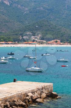 Pleasure motor boats and sailing yachts anchored in azure bay near sandy beach of mountainous Mediterranean island Corsica