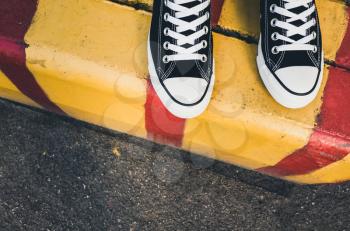 Black and white new sneakers, teenager feet stand on yellow red urban road border. Closeup photo with selective focus