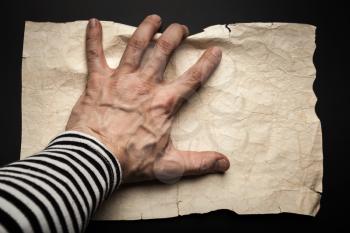 Sailor hand catching empty old crumpled paper sheet over black background, pirate map concept