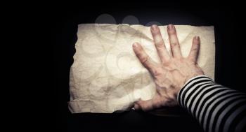 Strong sailor hand catching empty old crumpled paper sheet on black background, pirate map concept